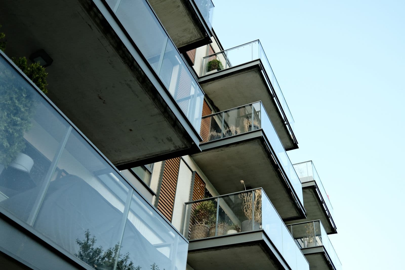 Cam korkuluklu balkonlara sahip modern apartman cephesinin açık mavi gökyüzü altında alttan görünümü