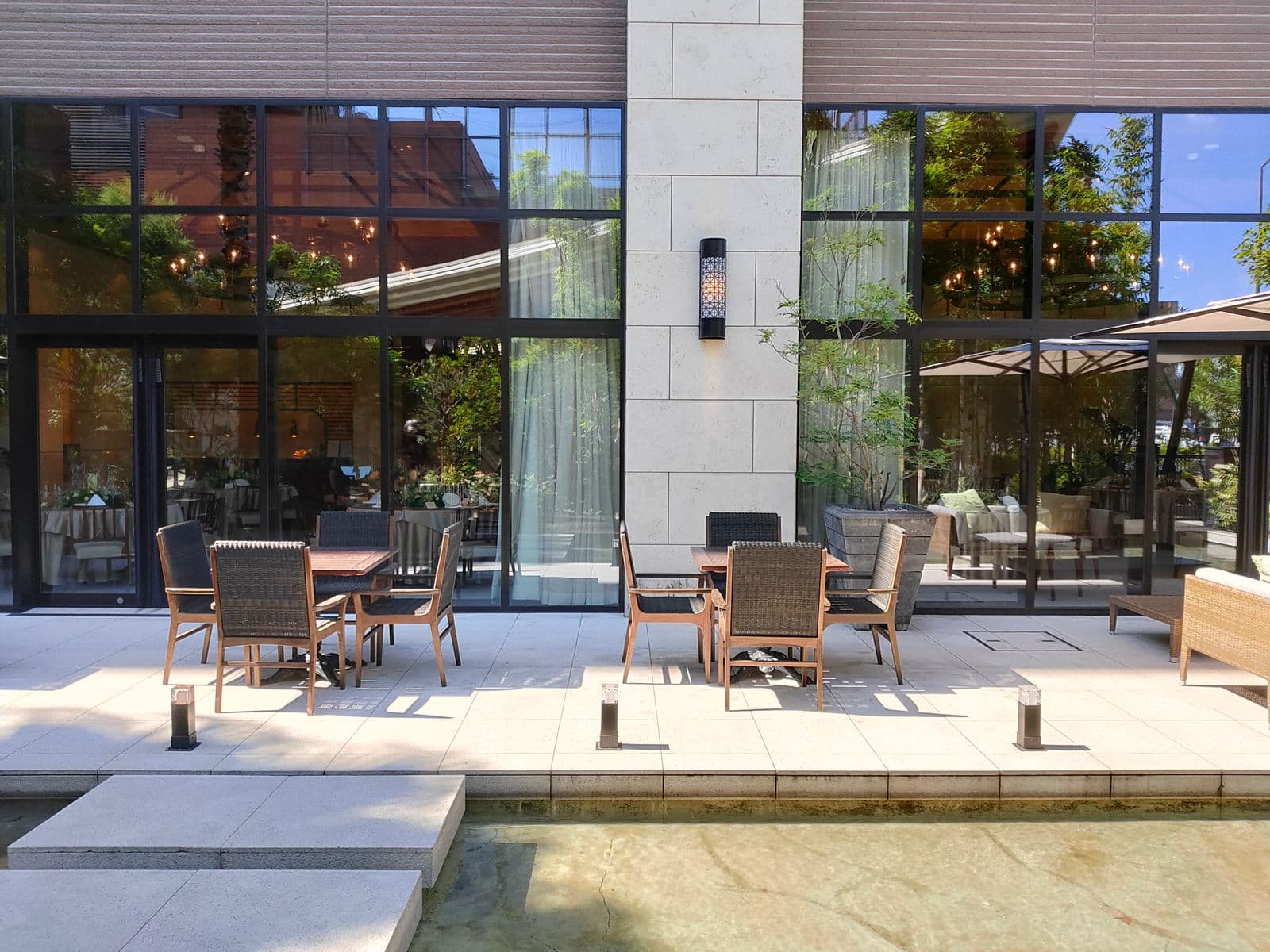 Geniş cam duvarlı bir mekanın önünde hasır sandalyeli masaların dizildiği güneşli restoran terası