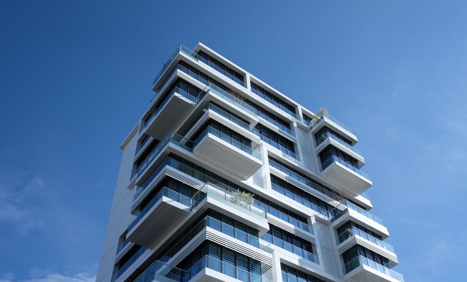 Masmavi gökyüzü altında cam balkon korkuluklu modern beyaz apartman