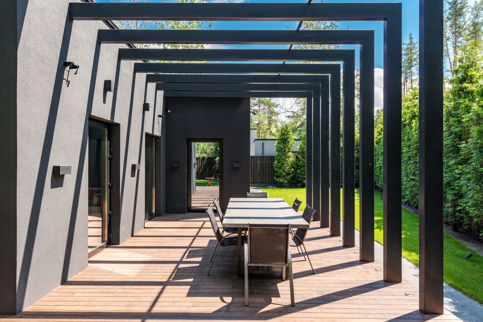 Bahçeli evin terasını kapatan antrasit profilli modern pergola