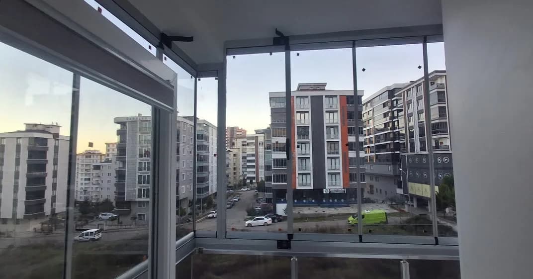 Balkona uygulanmış çerçevesiz katlanır cam balkon sistemi, içeriden site manzarası